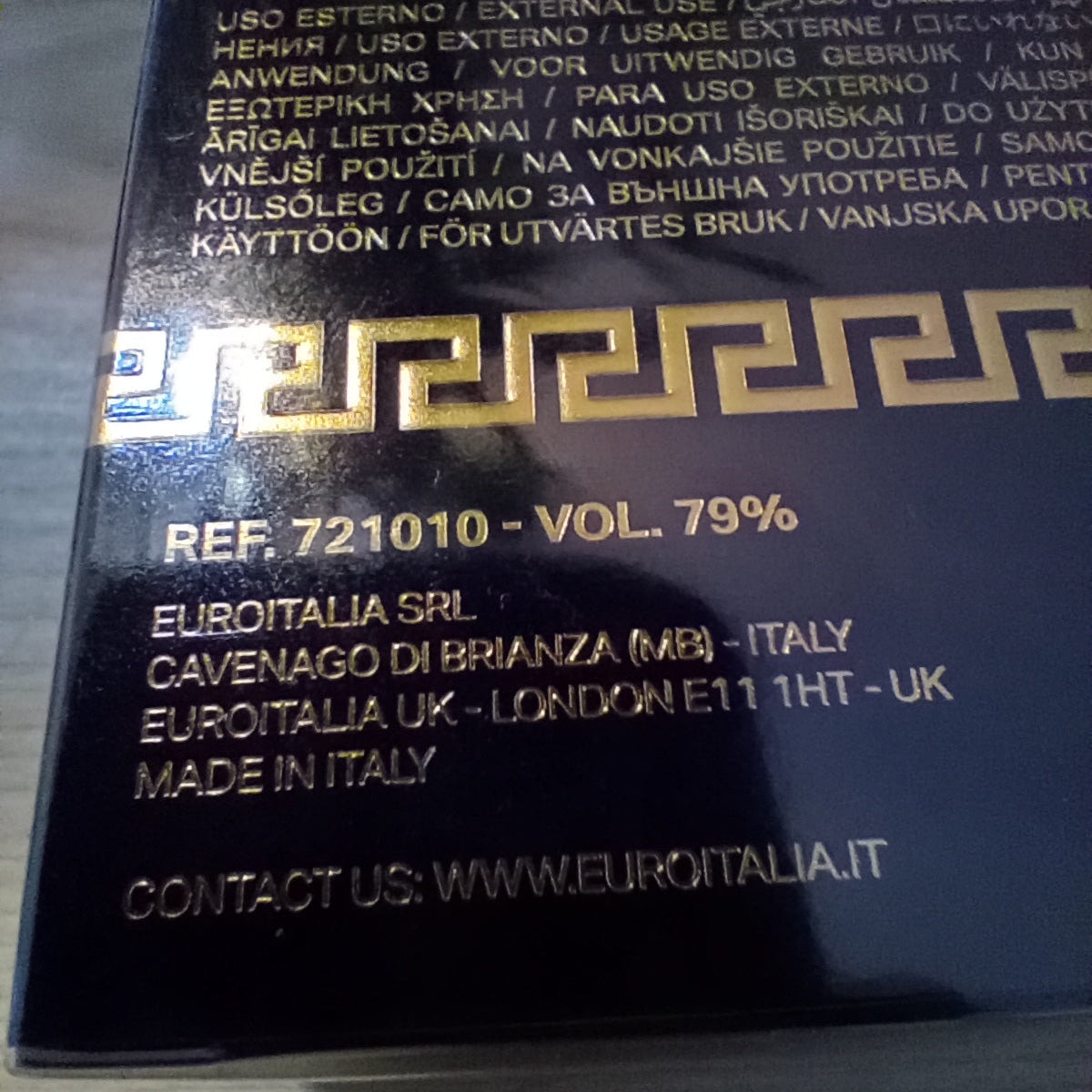 Close-up of the back of a black cosmetic box with gold text and a gold Greek key border, showing product reference, volume, manufacturer details for EuroItalia Srl, and a website.