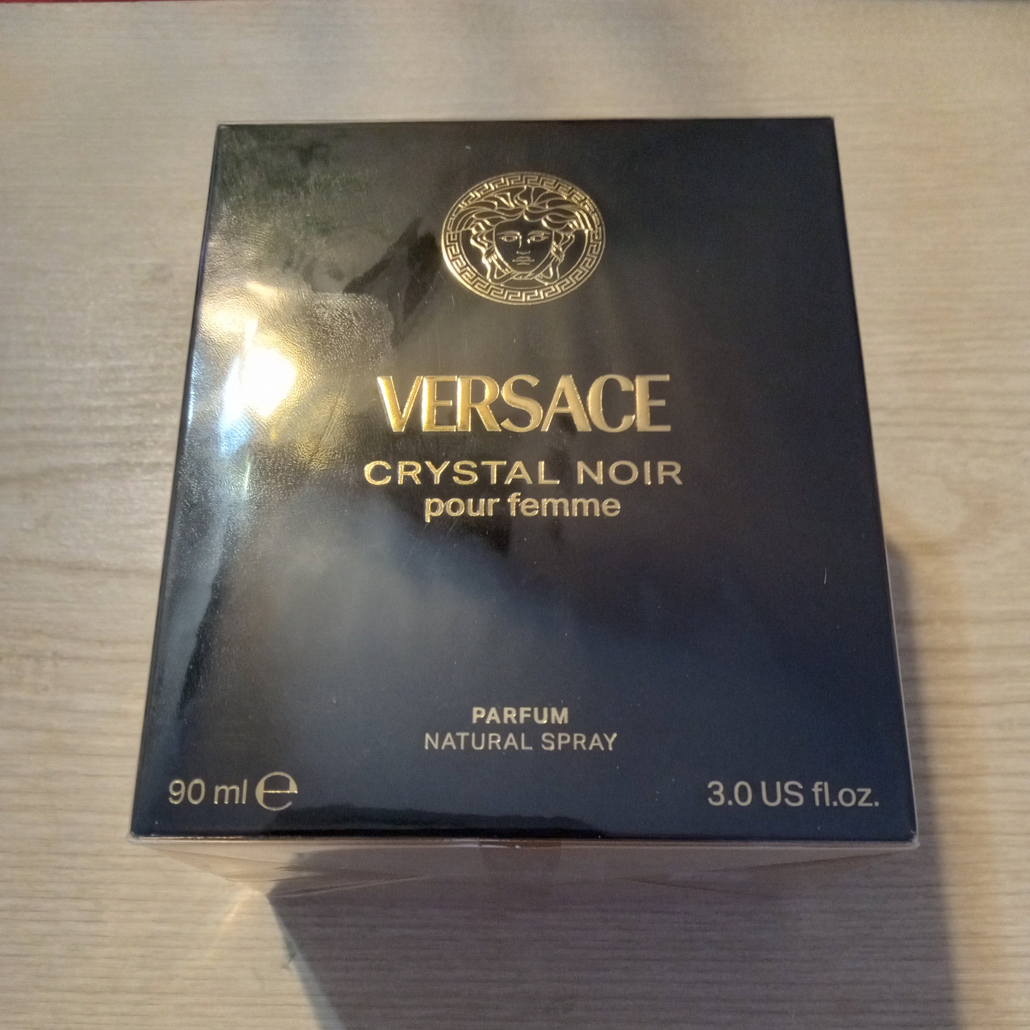 Versace Crystal Noir pour femme perfume box in black with gold lettering and logo, placed on a light wood surface.